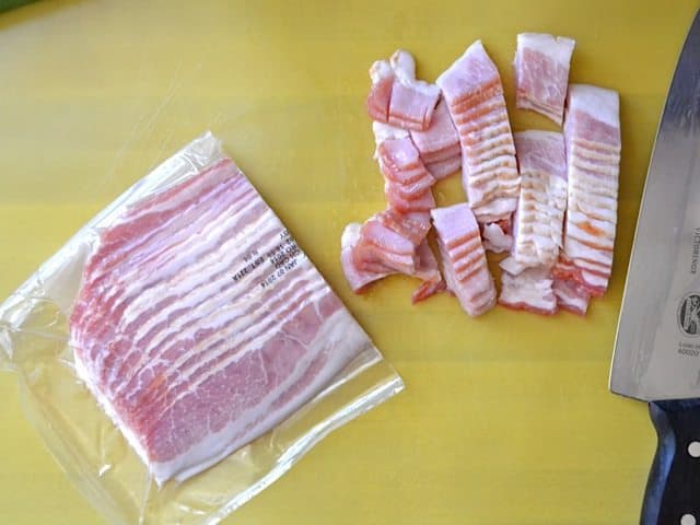 Bacon being chopped up with knife on cutting board 