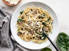 A shallow bowl full of Spinach and Artichoke One Pot Pasta with spinach and feta on the sides.