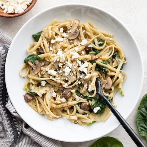 A shallow bowl full of Spinach and Artichoke One Pot Pasta with spinach and feta on the sides.