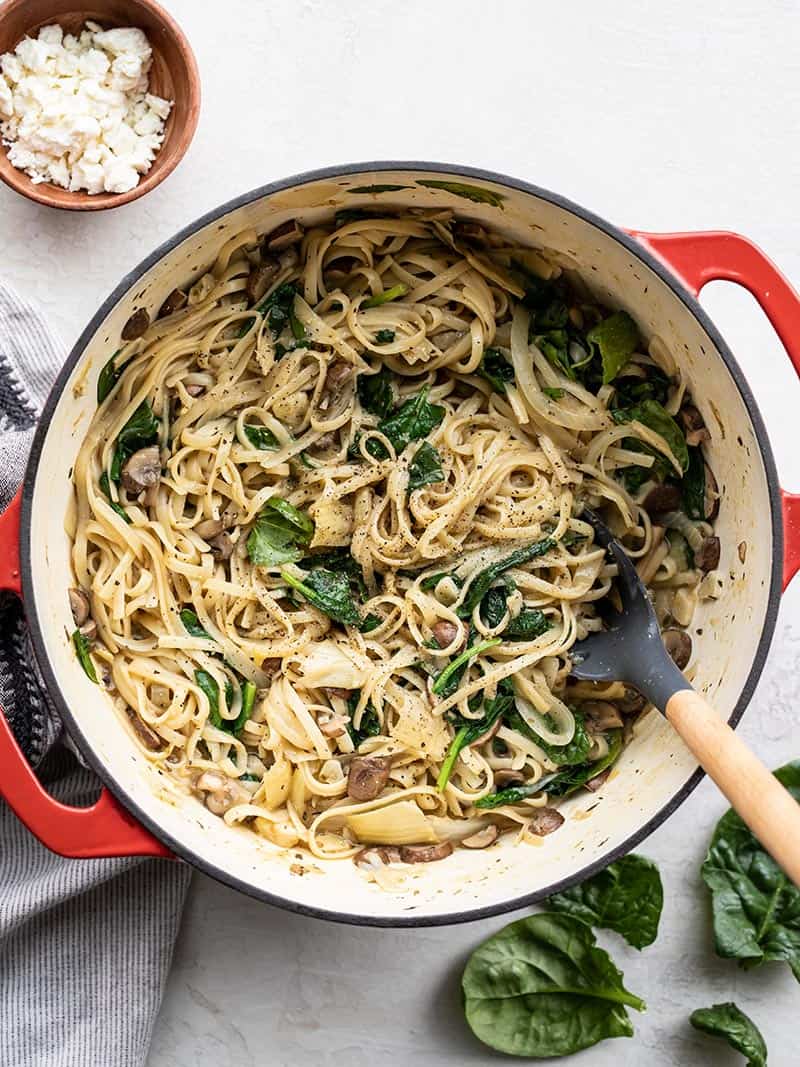 A red Dutch oven full of Spinach and Artichoke Wonderpot, with feta and spinach leaves on the sides