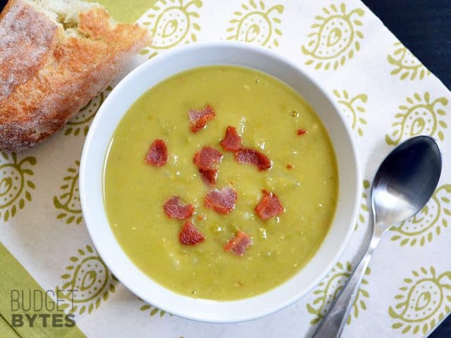 Top view of a bowl of Split Pea Bacon & Potato Soup with a spoon and piece of bread on the side 