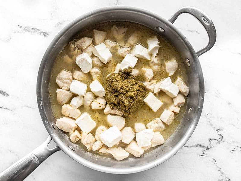pesto and cream cheese added to the skillet with the chicken and broth