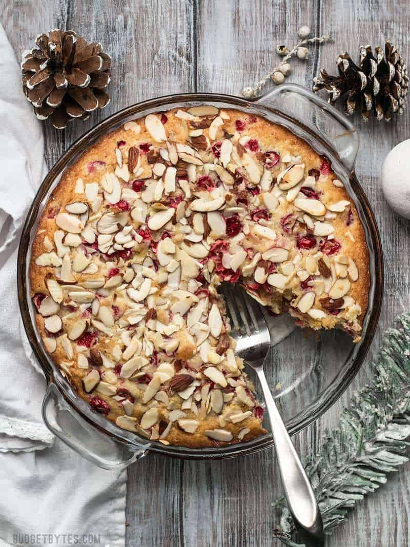 Top view of a Cranberry Almond Cake with one slice taken out, pine cones in background for staging 