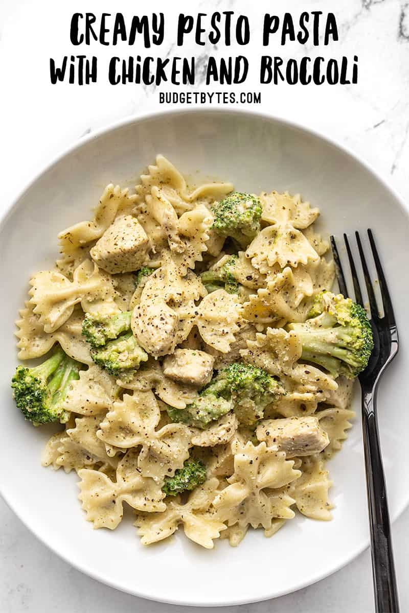 A bowl full of creamy pesto pasta with chicken and broccoli, a black fork in the side