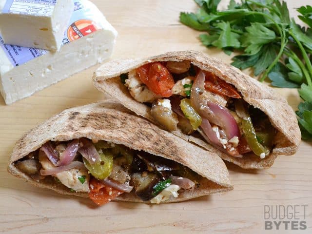 Two halves of a Greek Stuffed Pita, cilantro and feta cheese in the background 