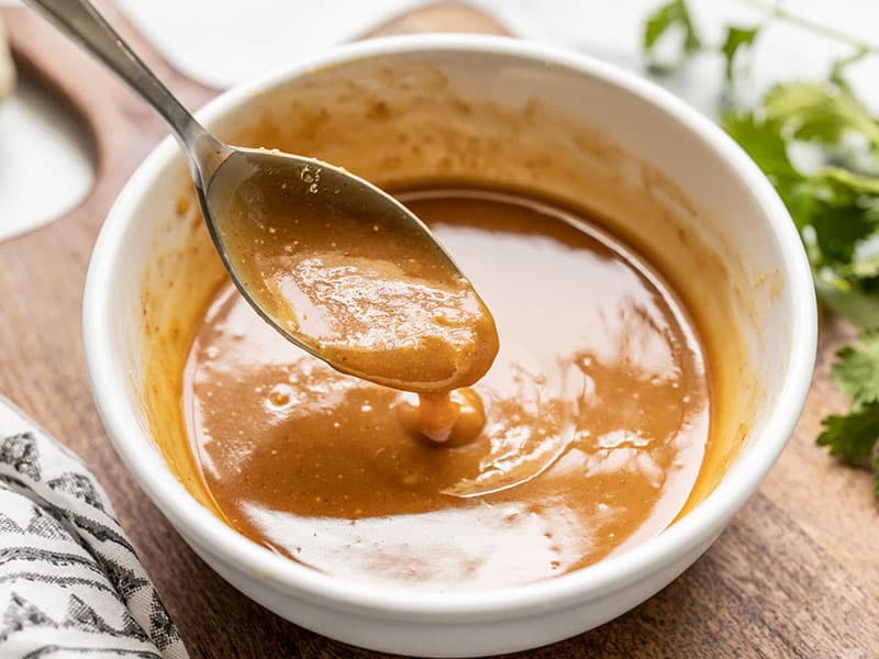Front view of peanut lime dressing dripping off a spoon into a bowl.