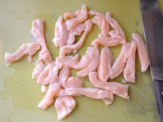 Chicken sliced into thin strips with knife 
