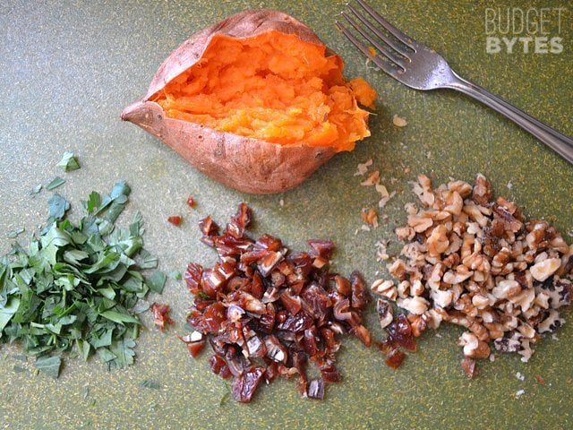 One baked sweet potato cut open with piles of toppings to put on top 