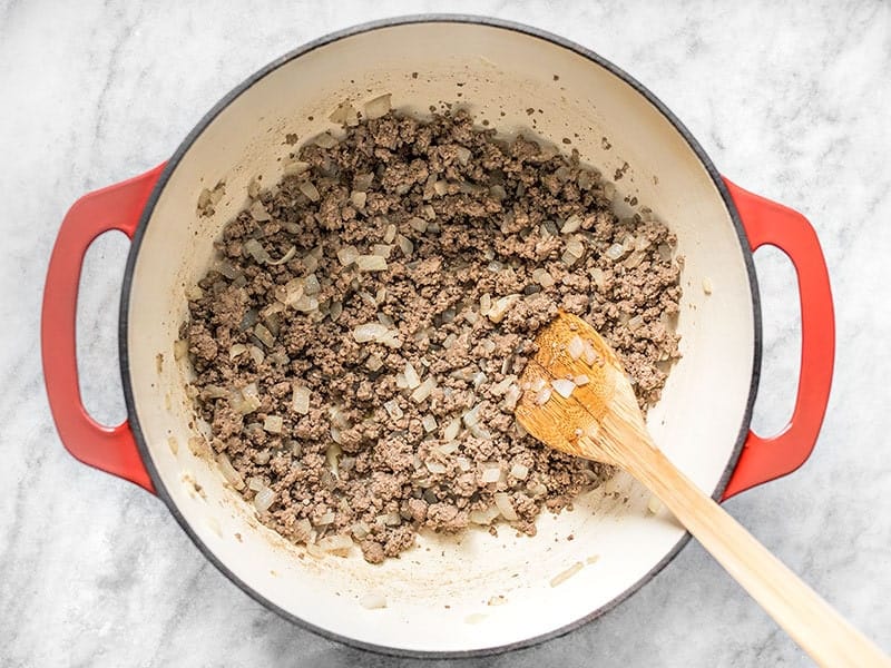 Browned beef in a dutch oven with a wooden spoon