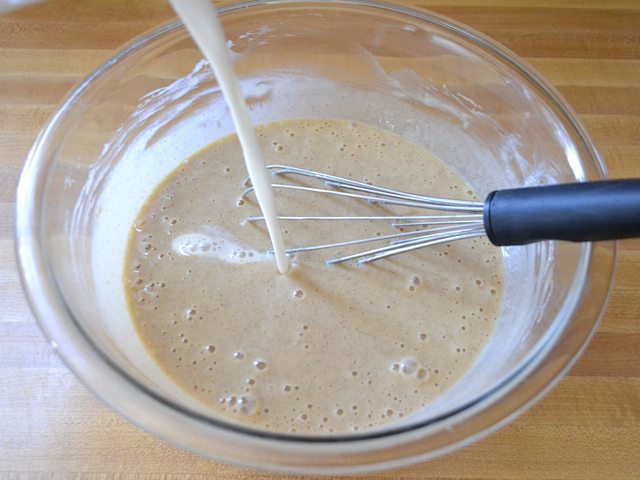 Milk being poured into other ingredients in mixing bowl  with whisk 