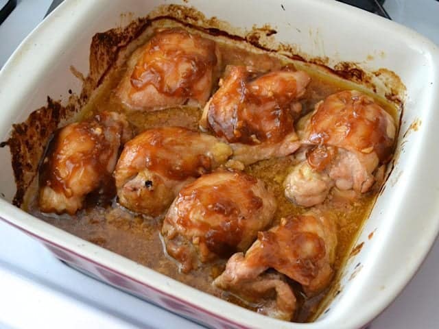 Extra sauce poured over top of cooked chicken thighs in baking pan 