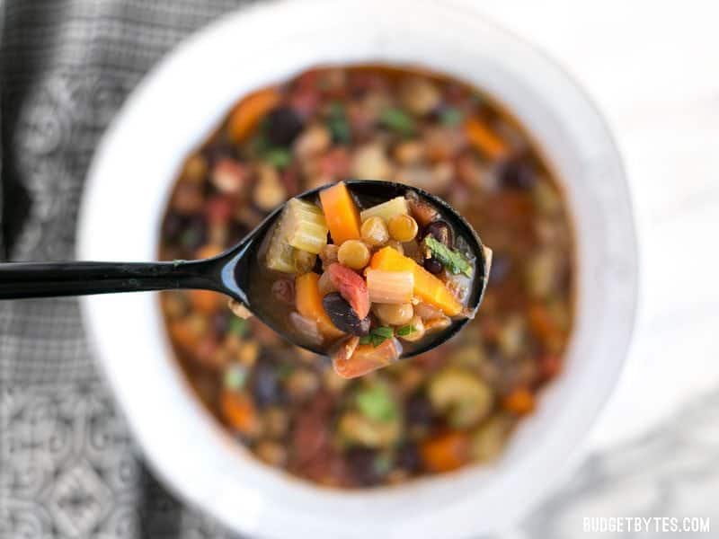 Spoonful of Chunky Lentil and Vegetable Soup being held over bowl 