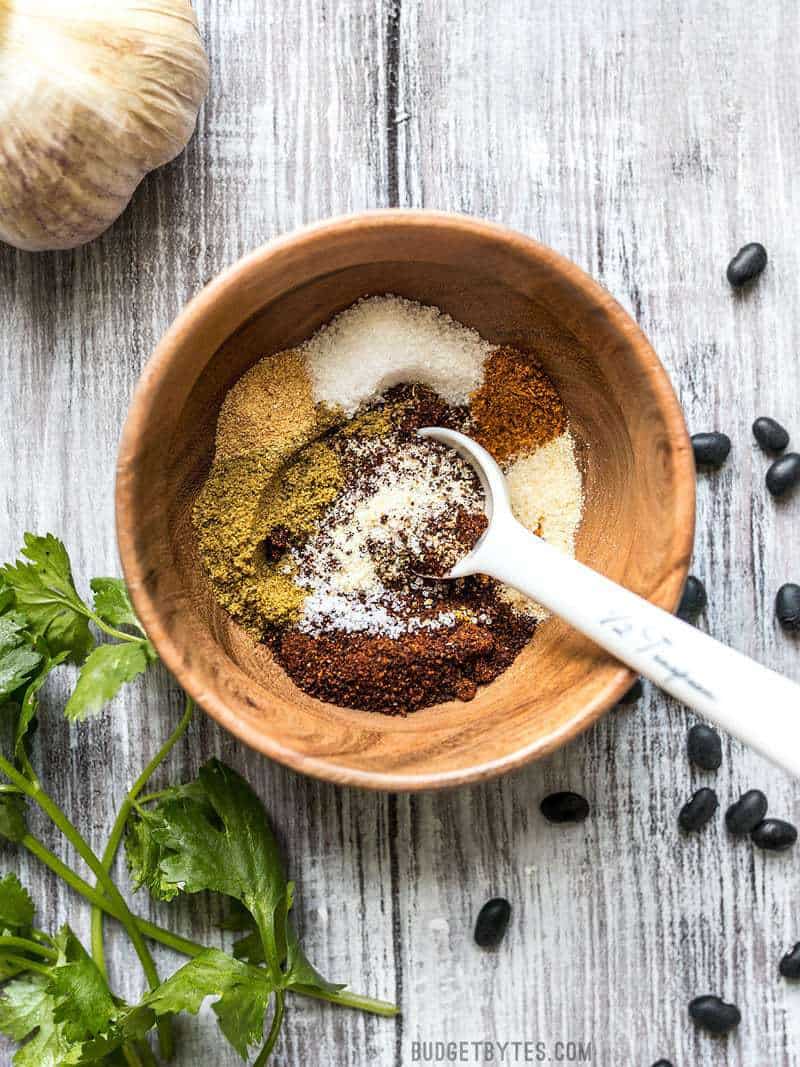 A bowl of homemade chili seasoning being stirred together on a wooden background.