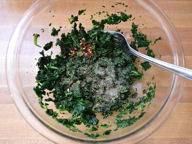 Seasoning mixed into frozen spinach  in mixing bowl with fork 
