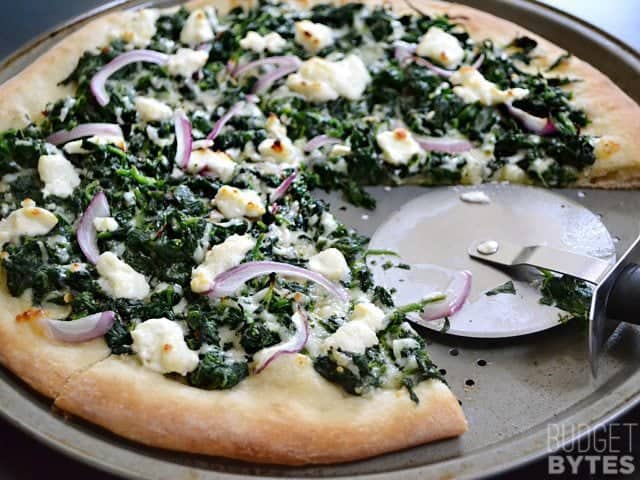 Easy White Spinach Pizza with one slice taken out and pizza cutter cutting the rest 