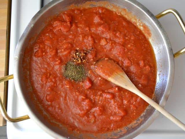 seasoning and tomatoes added to garlic in pan