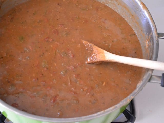 Smashed cooked beans in pot, mixed together with wooden spoon 