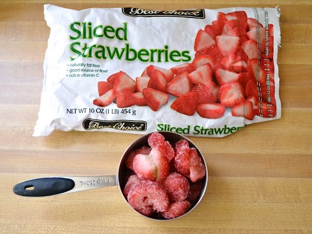 Bag of frozen sliced strawberries with a measuring cup full of them 