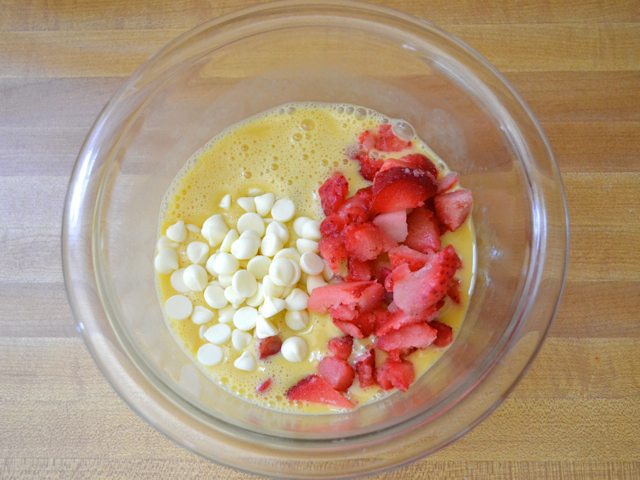 Strawberries and white chocolate chips added to mixed egg mixture in mixing bowl 