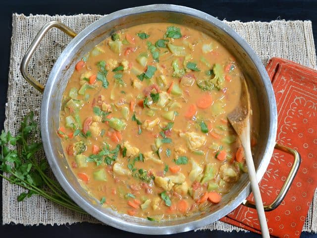 Top view of a pot of Coconut Vegetable Curry with a wooden spoon 