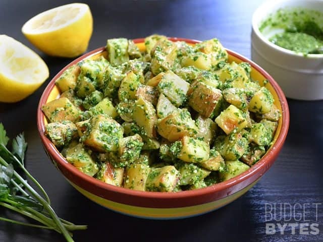 Side view of a bowl of Parsley Pesto Potatoes, parsley and lemon halves on the side 