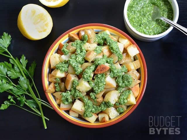 Top view of a bowl of Parsley Pesto Potatoes, parsley, lemon halves and a small bowl of pesto on the side 