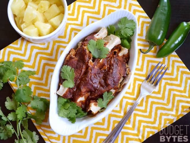 Top view of a dish of Beef & Pineapple Enchiladas with a bowl of pineapple, cilantro and jalapeños on the side 