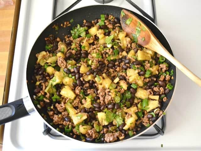 Enchilada filling stirred together in skillet with wooden spoon 