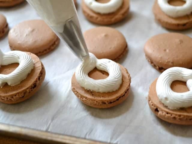 Pastry bag filled with marshmallow mixture being piped onto meringue circles 