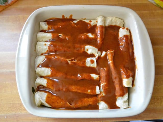 Dish filled with rolled enchiladas and sauce poured over the top, ready to bake 