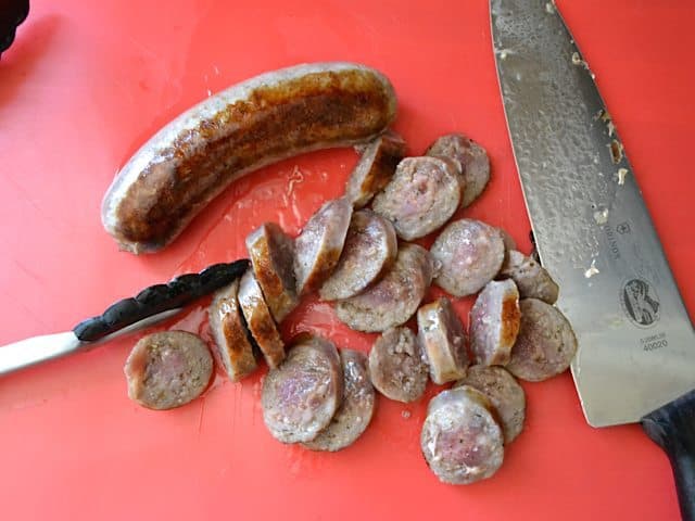 Cooked sausage being cut into slices with knife 