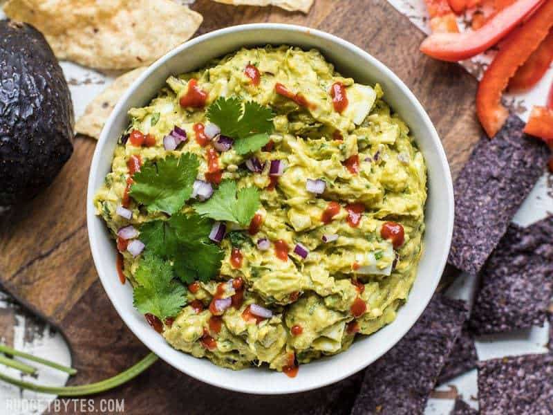 Top view of a bowl of finished loaded guacamole garnished with cilantro and sriracha