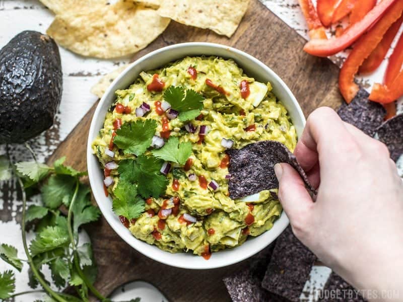 Top view of a chip being dipped into a bowl of loaded guacamole. 