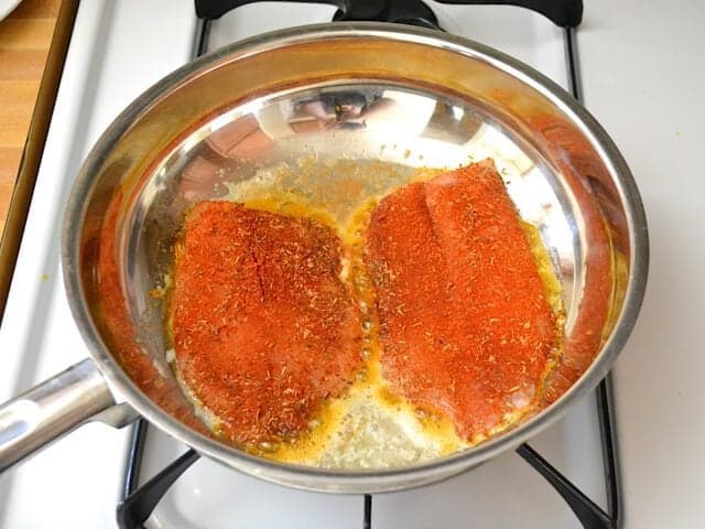 Two tilapia fillets cooking in skillet on stove top 