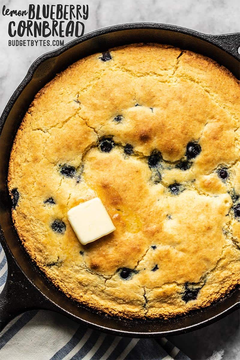 Close up of baked Lemon Blueberry Cornbread in a cast iron skillet with a pat of butter melting on the bottom side.