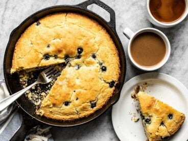 Lemon Blueberry Cornbread served on a plate next to the skillet and two mugs of coffee.
