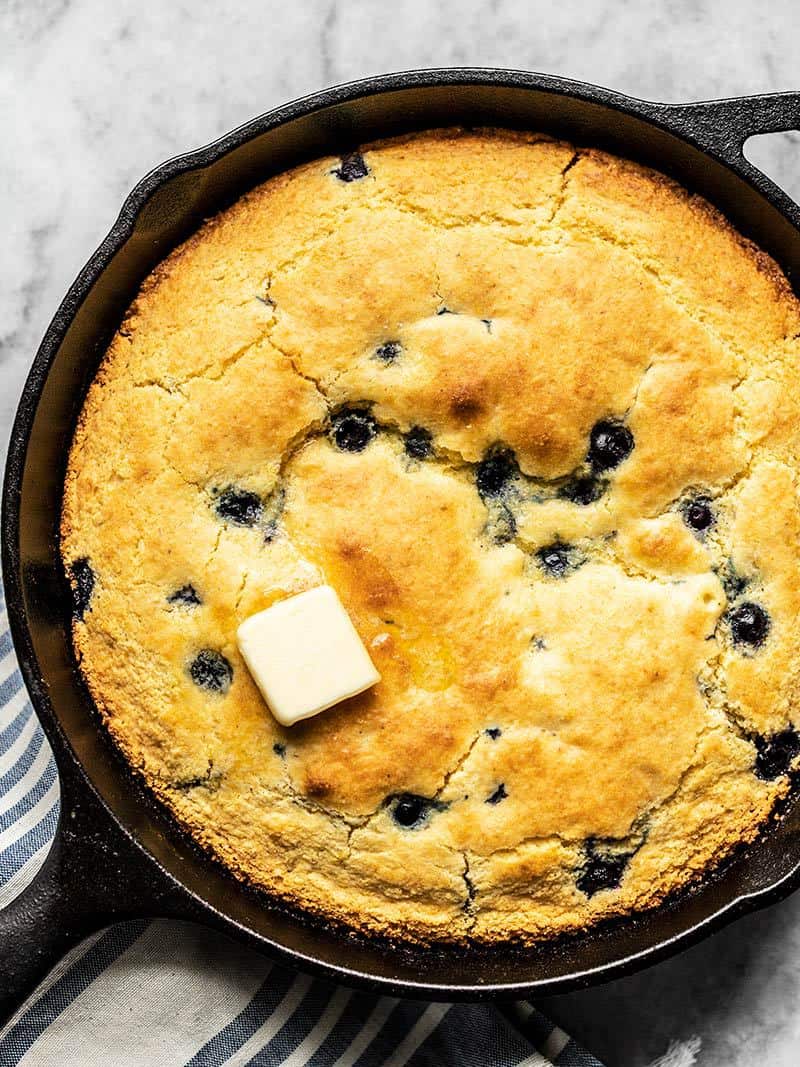 Close up of baked Lemon Blueberry Cornbread in a cast iron skillet with a pat of butter melting on top.