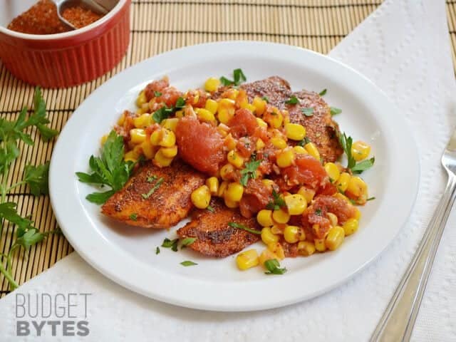 Top view of a plate of fish with Sautéed Corn and Tomatoes on top 