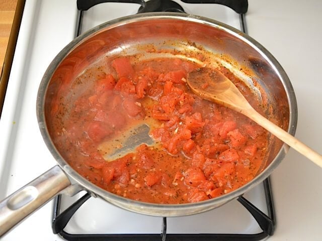 Simmering tomatoes in skillet with wooden spoon 