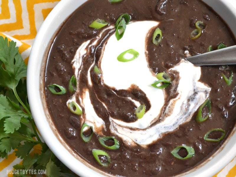Top view of a bowl of black bean soup garnished with green onion and sour cream