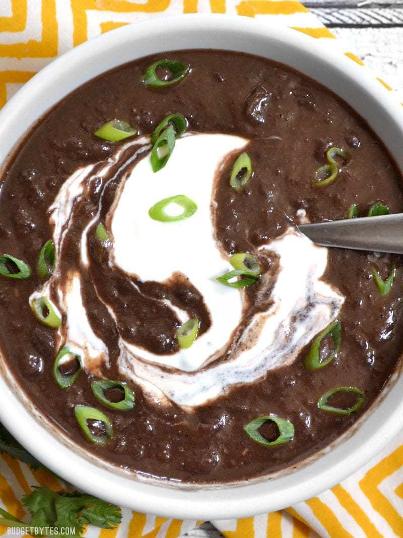 Top view of a bowl of black bean soup garnished with green onions and sour cream