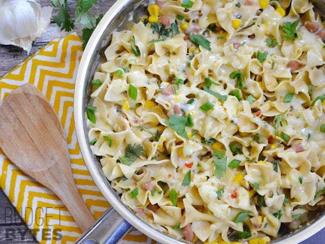 Top view of a skillet of Creamy Vegetarian Enchilada Pasta with a wooden spoon and a yellow chevron napkin on the side 