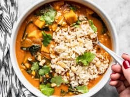 A hand scooping up a spoonful of Vegan West African Peanut Stew with Rice