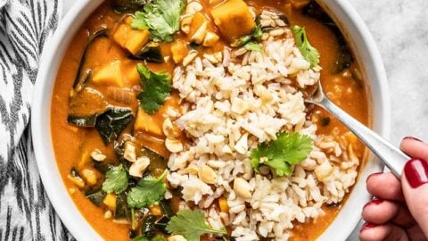 A hand scooping up a spoonful of Vegan West African Peanut Stew with Rice