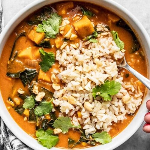 A hand scooping up a spoonful of Vegan West African Peanut Stew with Rice