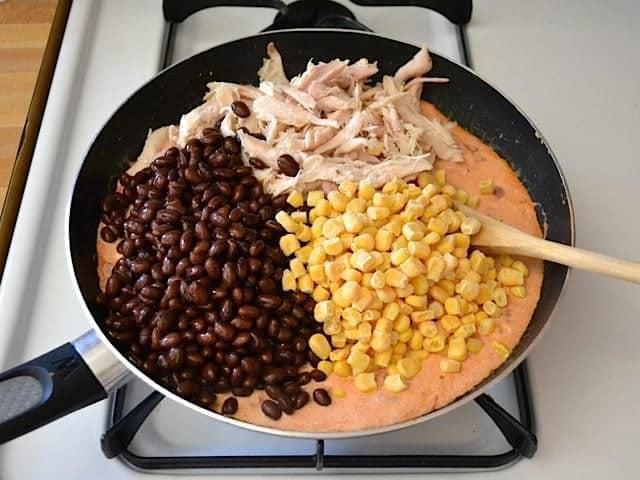 Shredded chicken, black beans and corn added to tomato sauce in skillet 