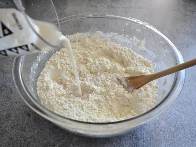 Pouring wt ingredients into dry ingredients in mixing bowl with wooden spoon