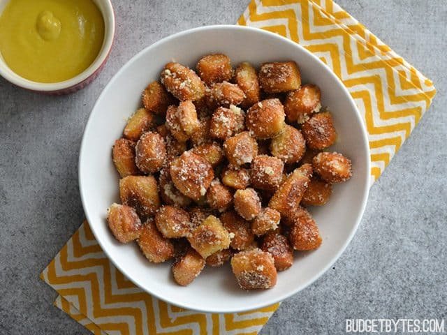 A bowl of Parmesan Garlic Pretzel Bites on a yellow chevron napkin with a small bowl if mustard on the side 