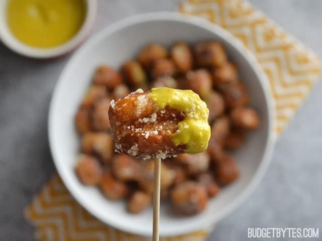 Close up of a Parmesan Garlic Pretzel Bite dipped in mustard, on a toothpick