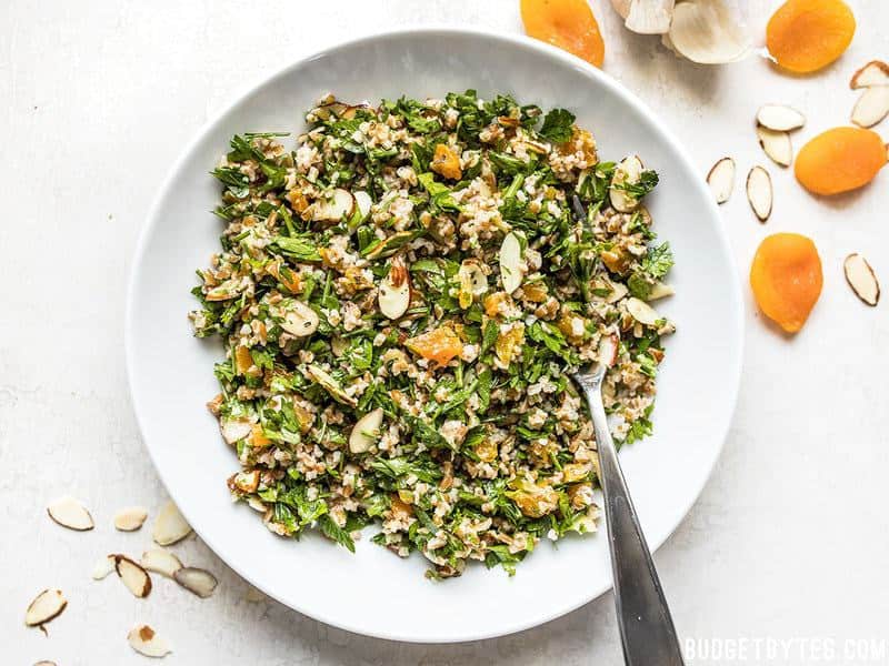 Top view of a bowl of Parsley Salad with Almonds and Apricots, almonds and apricots on side for staging 